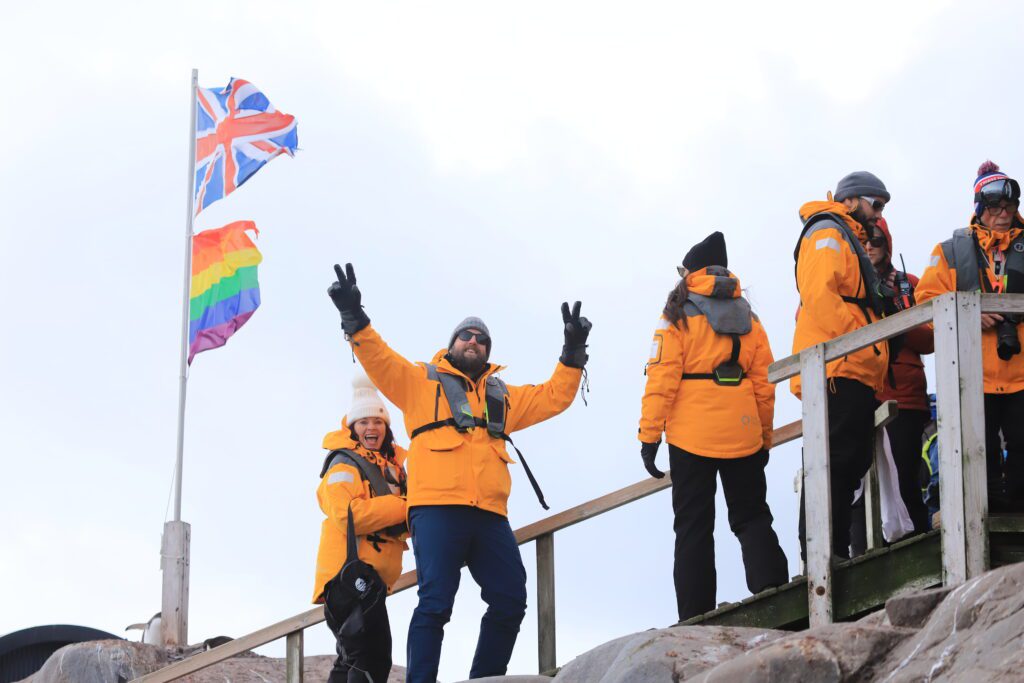 Duncan Greenfield-Turk on a travel journey with Quark, standing under the Pride Flag and Union Jack in Antarctica
